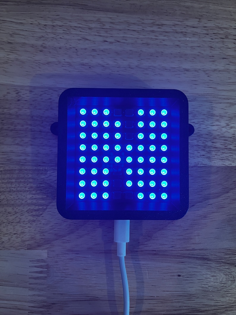 May include: A black square-shaped device with a grid of blue LED lights. The device is plugged into a white USB cable.