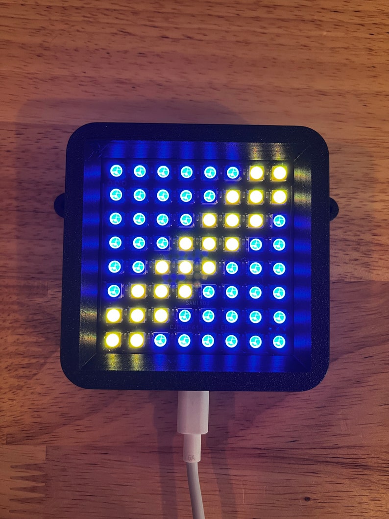 May include: A black square-shaped device with a grid of blue and yellow lights. The device is plugged into a white cord.