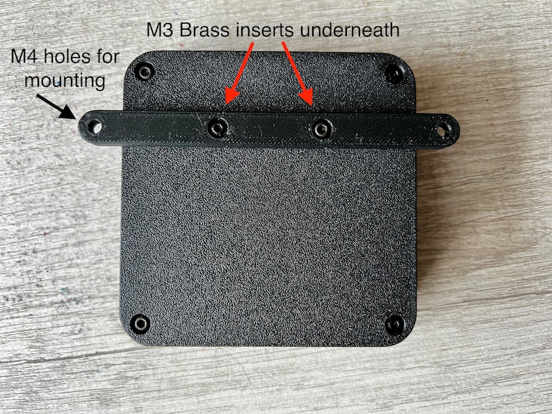 May include: Black plastic square with four M4 holes for mounting. The top edge has a black plastic bar with two visible M3 brass inserts underneath.