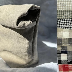 May include: A beige linen fabric lunch bag with a folded top. The bag is sitting on a white surface. The image also shows a variety of fabric swatches with different patterns and colors, including natural checks, white/black stripes, peak green checks, powder blue checks, dark blue checks, bio green checks, black/beige checks, and natural/red checks.