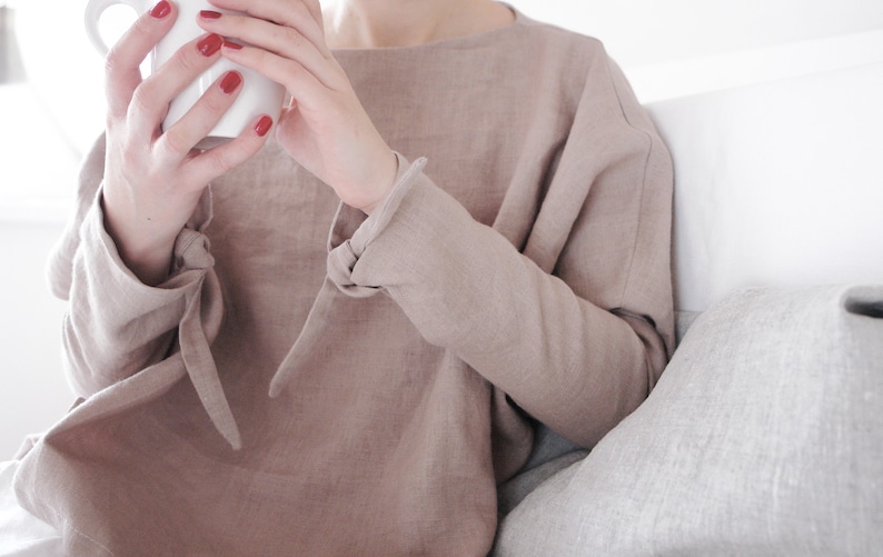 Minimalist linen kimono-style top in a neutral beige tone. Features long sleeves with delicate tie details at the wrists and a relaxed, oversized fit. Made from breathable, high-quality linen for effortless comfort and style