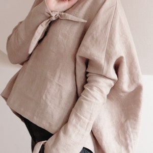 Elegant oversized linen kimono top in a soft beige color. Designed with wide, draped sleeves for a relaxed fit and stylish tie details at the wrists. Crafted from breathable, natural linen for a lightweight and comfortable feel.