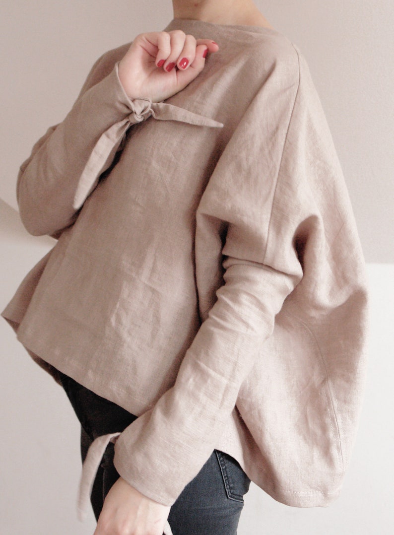 Elegant oversized linen kimono top in a soft beige color. Designed with wide, draped sleeves for a relaxed fit and stylish tie details at the wrists. Crafted from breathable, natural linen for a lightweight and comfortable feel.