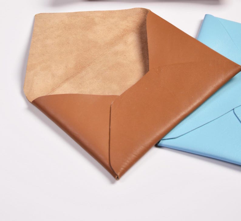 Puede incluir: Tres sobres de cuero en diferentes colores: marr&oacute;n, azul y beige. El sobre marr&oacute;n est&aacute; abierto, revelando un interior beige.