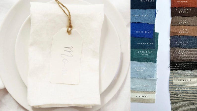 May include: A white linen napkin with a white tag that says "Mon" on it. The napkin is on a white plate. The image is a close-up of the napkin and tag.