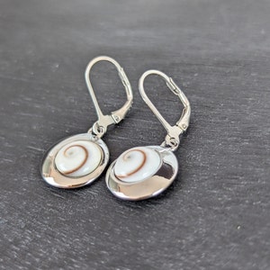 Könnte beinhalten: Ein Paar silberne Ohrringe mit einem weißen und braunen Muschel-Design. Die Ohrringe haben einen Bügelverschluss.