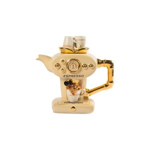 Puede incluir: Una tetera de cerámica blanca con forma de máquina de espresso con detalles dorados. La tetera tiene un medidor que indica "TEA" y una taza pequeña con un diseño marrón y blanco. La tetera dice "ESPRESSO" en la parte delantera.