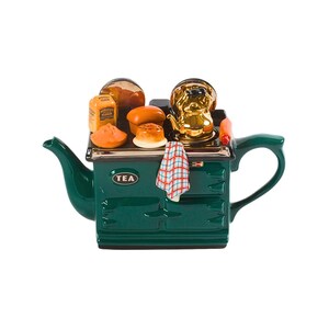 May include: A green ceramic teapot shaped like a vintage stove with a gold kettle, bread, and flour on top. The teapot has a "TEA" label and a red and white checked tea towel hanging on the side.