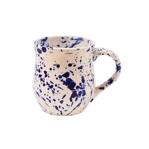 May include: A white ceramic mug with a blue splatter paint design. The mug has a rounded body and a handle.