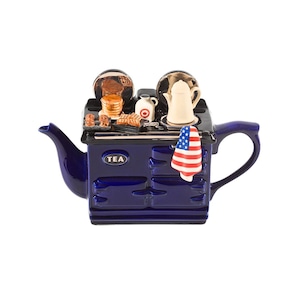 Könnte beinhalten: Eine marineblaue Teekanne in Form eines Ofens, mit Griff und Ausguss. Auf der Herdplatte befinden sich Miniatur-Lebensmittel, eine weiße Teekanne und eine kleine amerikanische Flagge. Das Wort "TEA" ist auf der Vorderseite aufgedruckt.