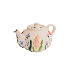 May include: A white ceramic teapot with a floral design. The teapot features a variety of flowers in shades of blue, pink, orange, and green.