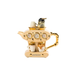 Op de afbeelding: Een witte theepot van keramiek in de vorm van een espressomachine met gouden accenten. De theepot heeft een klok, meters en twee kleine kopjes aan de voorkant. De tekst "ESPRESSO" staat op de voorkant van de theepot.
