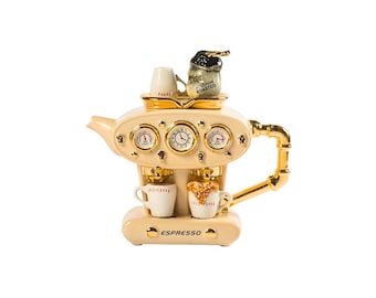 Puede incluir: Una tetera de cerámica blanca con forma de máquina de espresso con detalles dorados. La tetera tiene un reloj, indicadores y dos tazas pequeñas en la parte delantera. El texto "ESPRESSO" está impreso en la parte delantera de la tetera.