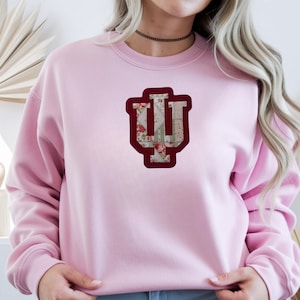 Puede incluir: Sudadera rosa claro con un diseño floral y granate "IU". Las letras están delineadas en granate y rellenas con un estampado floral. La sudadera es de estilo casual.