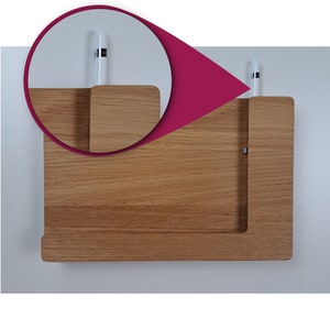 May include: A wooden wall-mounted organizer with two slots for holding styluses or pens. The organizer is made of light brown wood and has a simple, modern design.