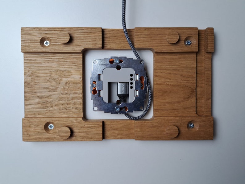 May include: A wooden wall plate with a metal electrical outlet box mounted in the center. The plate has a light brown finish and is designed to be installed on a wall.