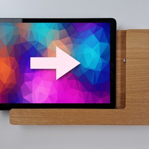 May include: A wooden stand with a tablet resting on top. The tablet has a colorful abstract background. An arrow points to the right.