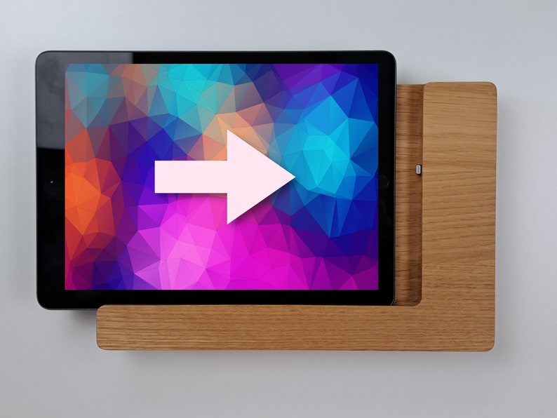May include: A wooden stand with a tablet resting on top. The tablet has a colorful abstract background. An arrow points to the right.