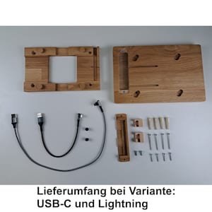 May include: A wooden phone stand with a cutout for a phone and a cable management system. The stand comes with two cables, screws, and mounting hardware. The text "Lieferumfang bei Variante: USB-C und Lightning" is visible in the image.