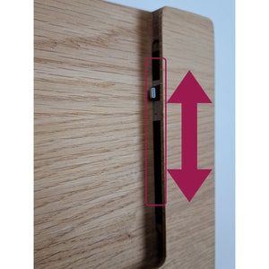 May include: A wooden stand with a slot that can be adjusted up and down to hold a device. The slot is made of dark wood and has a small metal piece on the side.