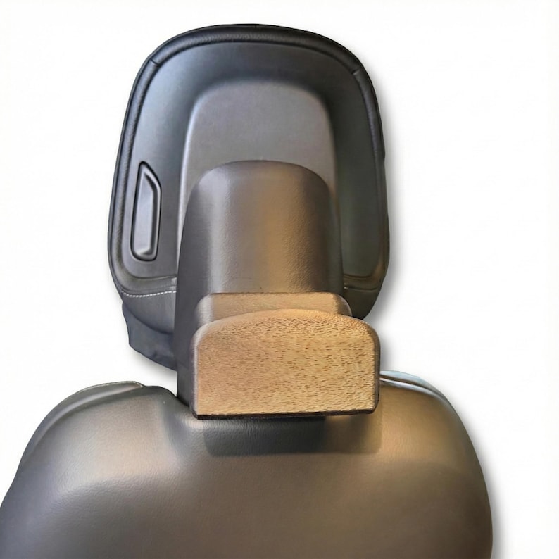 K&ouml;nnte beinhalten: Nahaufnahme einer schwarzen Auto-Kopfst&uuml;tze mit Holzakzent. Die Kopfst&uuml;tze besteht aus einem glatten, dunklen Material und hat ein rechteckiges Holzst&uuml;ck. Das Design ist modern und elegant.