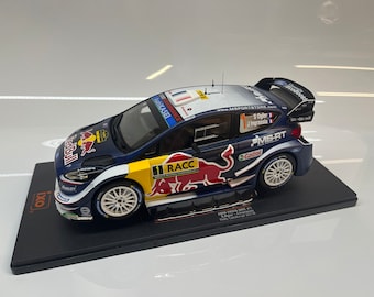 Op de afbeelding: Een blauwe en witte Ford Fiesta WRC #1 schaalmodel auto met Red Bull en Castrol logo's. De auto staat op een zwarte display basis met de tekst "Ford Fiesta WRC #1 S. Ogier J. Ingrassia Rally Catalunya 2018".