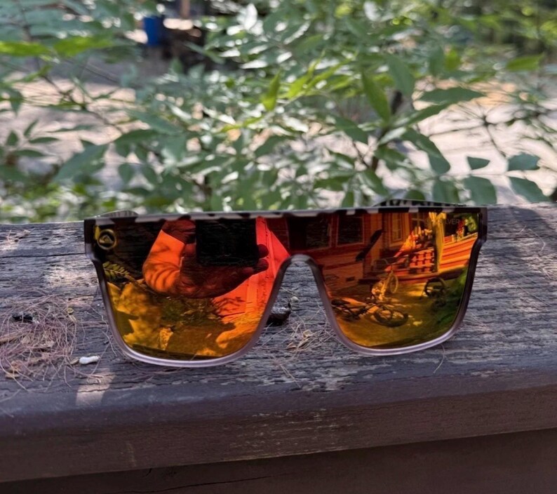 K&ouml;nnte beinhalten: Sonnenbrille mit flachem Rahmen im Schildpattmuster und reflektierenden, orange get&ouml;nten Gl&auml;sern. Die Gl&auml;ser haben eine spiegelnde Oberfl&auml;che, die die Umgebung reflektiert, und ein kleines Logo ist auf dem linken Glas zu sehen.