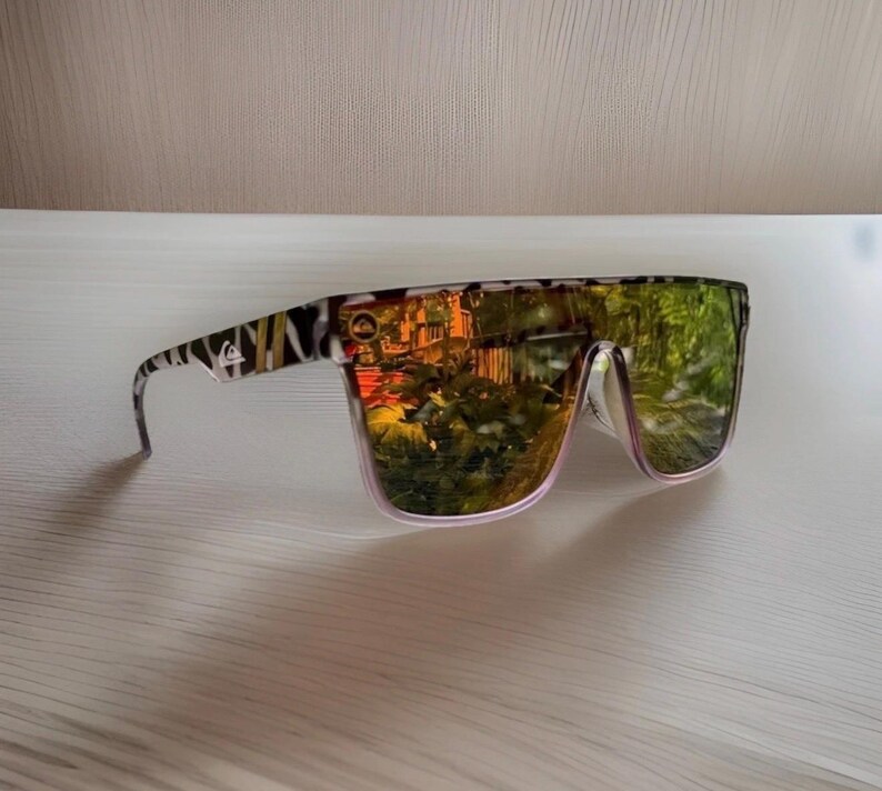 K&ouml;nnte beinhalten: Sonnenbrille im Shield-Design mit einem durchgehenden Glas in reflektierender Gold- und Gr&uuml;noptik. Der Rahmen ist an den B&uuml;geln mit einem schwarz-wei&szlig;en Tiermuster versehen, das zudem ein kleines wei&szlig;es Quiksilver-Logo aufweist.