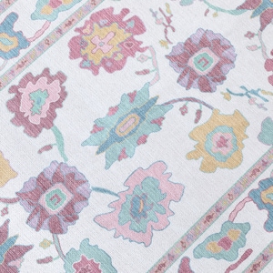 May include: A close-up of a white rug with a floral pattern. The rug features large flowers in shades of pink, purple, yellow, and blue, with green stems and leaves. The border has a repeating floral design.