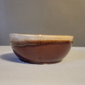 Puede incluir: Un tazón de cerámica marrón con un borde blanco. El tazón tiene un acabado esmaltado.
