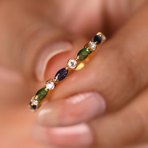 Puede incluir: Un anillo de oro con piedras preciosas alternas. El anillo presenta un patrón repetitivo de piedras azules, verdes y transparentes. Las piedras están engastadas en una banda de oro. Una joya delicada.