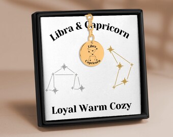 May include: Gold zodiac charm with the constellations for Libra and Capricorn. The charm is in a black box with a white background. The text on the box reads "Libra & Capricorn" and "Loyal Warm Cozy".