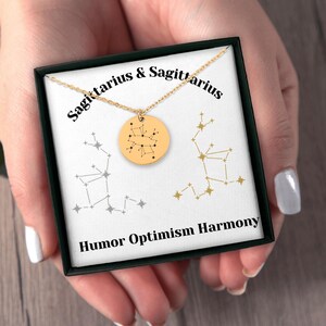 Könnte beinhalten: Eine goldene Halskette mit einem Anhänger der Sternbilder des Schützen in einer schwarzen Schachtel. Die Schachtel trägt den Text "Schütze & Schütze" und "Humor Optimismus Harmonie".