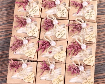 May include: A collection of small, brown cardboard boxes with clear windows. Each box contains a white, heart-shaped wooden tag with the text "Christine and Taylor" printed on it. The boxes are decorated with pink pearl beads, twine, and dried flowers.