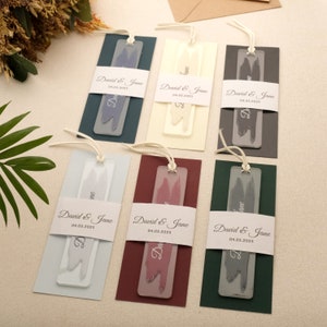 May include: A collection of personalized bookmarks in various colors. Each bookmark features a translucent rectangular tag with a brushstroke design and the names "David & Jane" along with the date "04.05.2025". The bookmarks have a string attached.