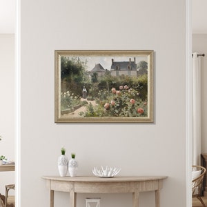 May include: A framed painting depicts a garden scene with a house in the background. The garden features a path, lush greenery, and blooming pink roses. A person in a long dress is walking in the garden. The painting is in a gold frame.