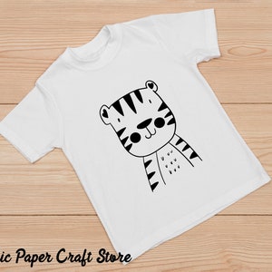 May include: White t-shirt with a black and white cartoon tiger design. The tiger has a cute expression and is wearing stripes.