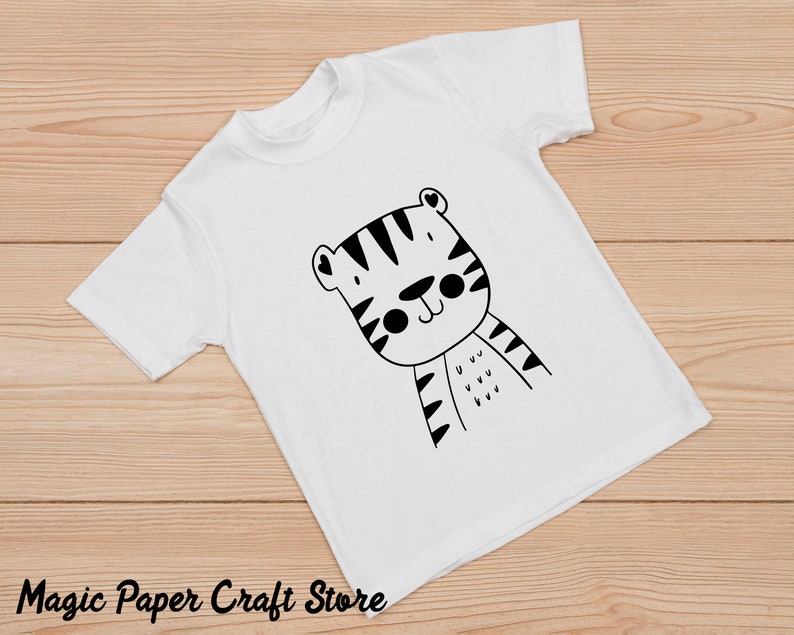 May include: White t-shirt with a black and white cartoon tiger design. The tiger has a cute expression and is wearing stripes.