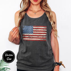 Puede incluir: Un top de tirantes gris carbón con un gráfico de bandera estadounidense desgastado. El top de tirantes se combina con pantalones cortos de ciclista negros.