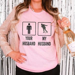 May include: Pink t-shirt with a graphic of two stick figures. The text reads "Your Husband" and "My Husband".