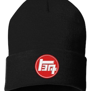 May include: A black knit beanie featuring a circular patch on the front cuff. The patch has a red background with a white stylized geometric logo in the center. The beanie is constructed from a ribbed fabric and has a folded brim design.