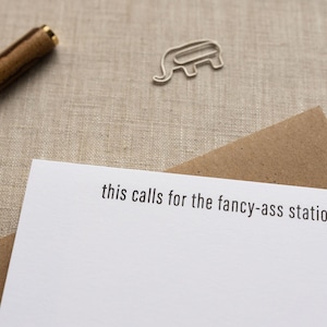 May include: A white card with the text "this calls for the fancy-ass stationery" printed on it. The card is sitting on a brown envelope.