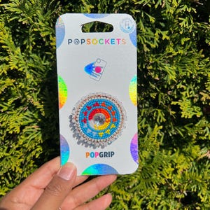May include: A colorful beaded phone grip with a white background and the text "PopSockets" and "PopGrip".
