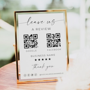 Puede incluir: Un letrero con marco dorado con el texto "leave us a review" y dos códigos QR para Google y Facebook. El letrero también incluye un nombre comercial, una calificación por estrellas y un mensaje de "gracias", junto con iconos de redes sociales y un identificador.