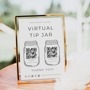 May include: A gold-framed sign with the words "Virtual Tip Jar" and two QR codes for Venmo and CashApp. The sign also includes the text "Thank You!" and social media icons. The sign is on a wooden surface.