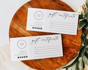 May include: Two white gift certificate cards with a minimalist design. The cards feature a circle with the text "LOGO HERE" and the text "gift certificate" in a handwritten font. The cards have lines for the recipient, giver, amount, and expiration date. The cards are on a wooden surface.