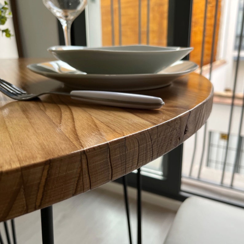 Detalle de mesa redonda de madera hecha a medida en madera maciza natural. La luz entra por la derecha.
Se ven los platos y un tenedor.