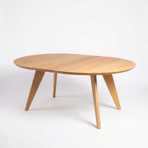 Op de afbeelding: Ovale salontafel van lichtkleurig hout met vier schuine poten. De tafel heeft een glad oppervlak en een modern, minimalistisch ontwerp. Geschikt voor een woonkamer of loungeruimte.