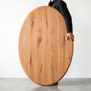 Peut inclure: Un grand plateau de table de forme ovale fabriqué en bois naturel brun clair avec un motif de grain visible. La surface présente des planches verticales assemblées, mettant en valeur des nœuds organiques et des variations de texture.