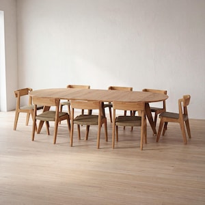Könnte beinhalten: Ein ovaler Esstisch aus hellem Holz, etwa 200 cm lang, umgeben von sechs passenden Stühlen. Die Stühle haben helle Holzrahmen und graue Sitzkissen. Der Tisch und die Stühle stehen auf einem hellen Holzboden.